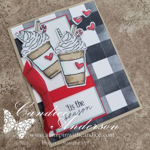 A holiday card featuring two coffee cups topped with whipped cream, hearts, and a festive ribbon on a buffalo check background.