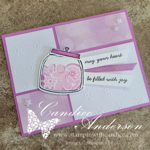 A festive handmade card featuring a jar filled with gingerbread cookies, decorated with pink accents and the sentiment 'may your heart be filled with joy.' The card has a collage-style layout with textured white and pink backgrounds.