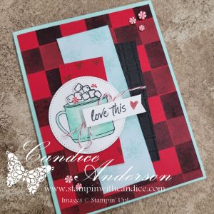 A handmade card featuring a faux Buffalo Check background in red and black, with a circular design showcasing a mug of cocoa topped with marshmallows, and the phrase 'love this' attached.