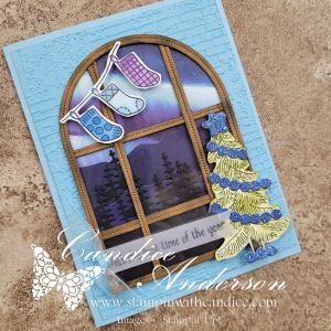 A handmade Christmas card featuring a window design with colorful stockings hanging, a serene winter scene visible through the window, and a decorated pine tree at the bottom.