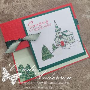 A handmade Christmas card featuring a church illustration with the text 'Seasons Greetings', surrounded by green trees and decorated with a ribbon.