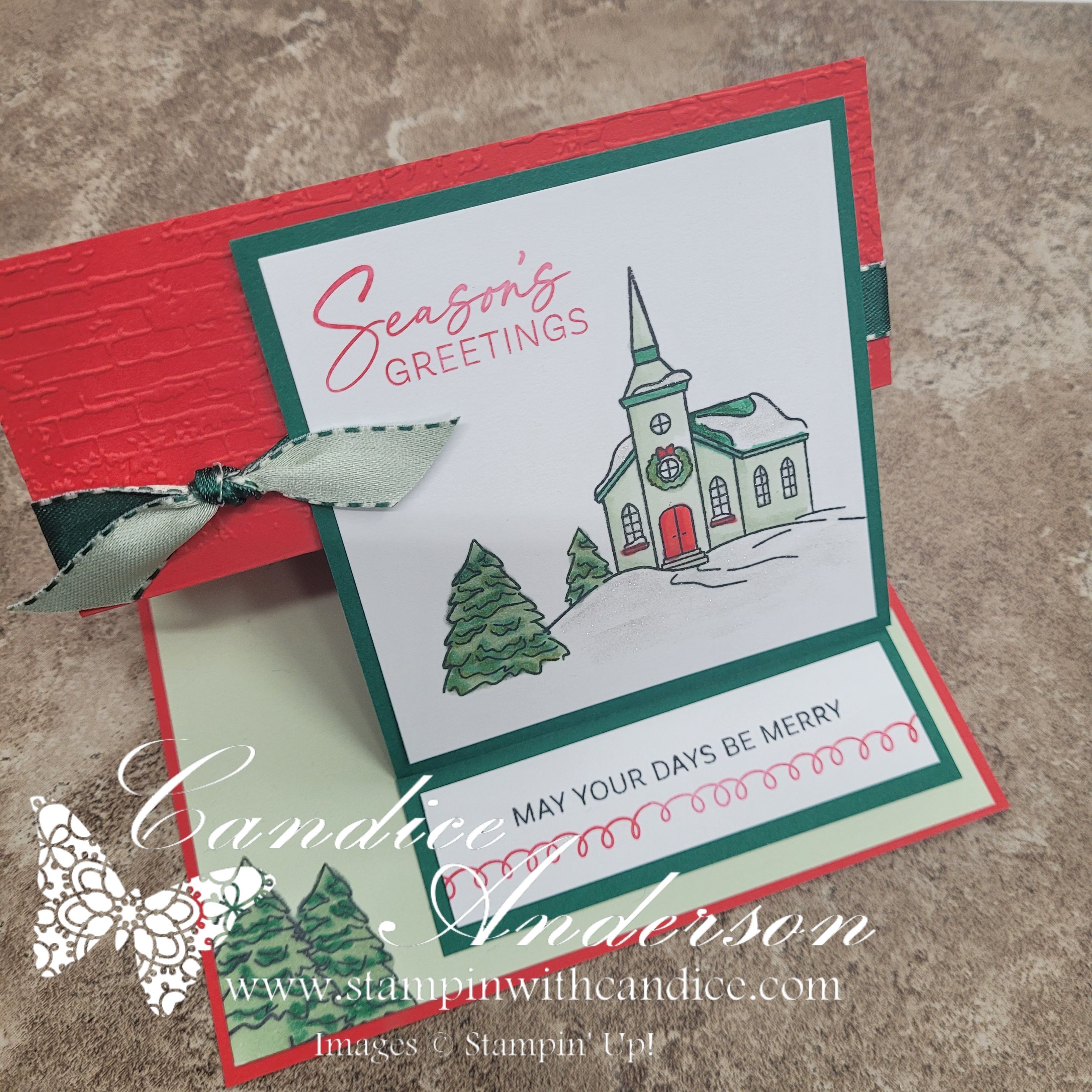 A festive reverse easel card featuring a church illustration and text that reads 'Season's Greetings' and 'May your days be merry'. The card is decorated with green and red colors, along with a ribbon.