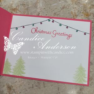 An inside view of a Christmas card featuring 'Christmas Greetings' text, colorful string lights, and soft green pine tree designs.