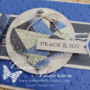 A handmade Christmas card featuring a decorative circular ornament shape with a mosaic pattern in shades of blue and silver glitter, accented with a 'Peace & Joy' sentiment tag and a twine bow.