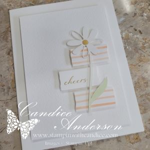 A handmade card featuring a daisy flower design with a striped background and the word 'cheers' printed on it.