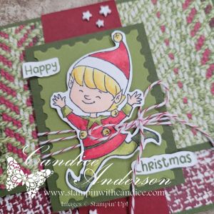 A festive handmade card featuring a cheerful elf character, surrounded by red and green decorative elements. The card includes the text 'Happy Christmas' and is embellished with twine and stars.