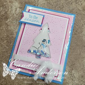 A festive card featuring a translucent tree design with a snowman in a winter scene, surrounded by colorful sequins, on a pink and blue background with the text 'tis the season' at the top.