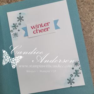 A greeting card featuring the phrase 'winter cheer' in bold red text on a light blue banner, surrounded by decorative snowflakes.