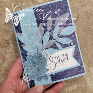 A handmade pop-up gift card holder featuring a floral design with embossed leaves and a 'TIS THE SEASON' greeting, set against a dark patterned background.