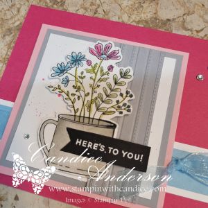 A floral card design featuring a colorful arrangement of flowers in a mug, set against a pink and gray background with a greeting that says 'HERE'S TO YOU!'