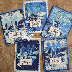 A collection of five handcrafted greeting cards featuring various shades of blue and white floral designs, with the text 'YOU MAKE ME SMILE' prominently displayed on each card.