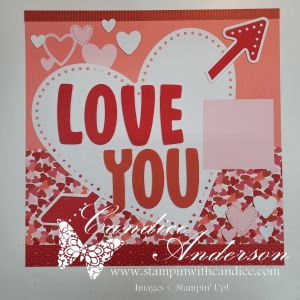 A scrapbook page featuring a large heart with the words 'LOVE YOU' prominently displayed, surrounded by decorative hearts and a pink square for photo placement.