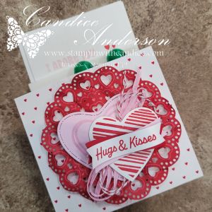 A decorative card featuring a lace-like red heart design with multiple smaller hearts, embellished with a pink and white striped heart that says 'Hugs & Kisses'.