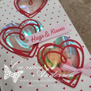 A handmade card featuring three red heart cutouts with iridescent backgrounds, accompanied by a pink 'Hugs & Kisses' sentiment and adorned with a pink ribbon.