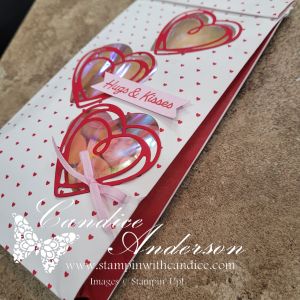 A handmade greeting card featuring three red heart cutouts with a transparent background, displaying colorful sequins inside, and the text 'Hugs & Kisses' on a pink ribbon.