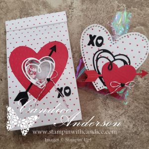A handcrafted gift box featuring red and white hearts with an arrow design, embellished with an 'XO' motif and colorful ribbons, presented on a textured background.