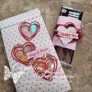 A decorated packaging with red hearts and the text 'Hugs & Kisses' holding colorful candies, next to a chocolate bar wrapped in pink paper with a tag that says 'I Adore You'.