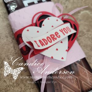 A decorative gift wrapper featuring hearts and the phrase 'I Adore You', on top of a chocolate bar.