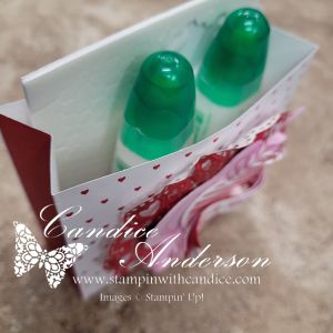 Two green-topped bottles of adhesive glue stored in a decorative holder with a pink and red design, featuring hearts.