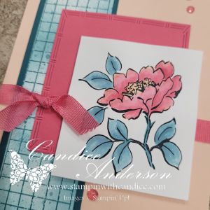 Close-up of a handmade card featuring a pink flower illustration with green leaves, placed on a textured pink background and accented with a pink ribbon.