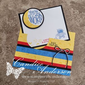A handmade birthday card featuring colorful striped paper in yellow, blue, and red, with an astronaut illustration. The top has a circular sentiment that says 'You're out of this world' and the inside includes 'Happy Birthday' and a date stamp.